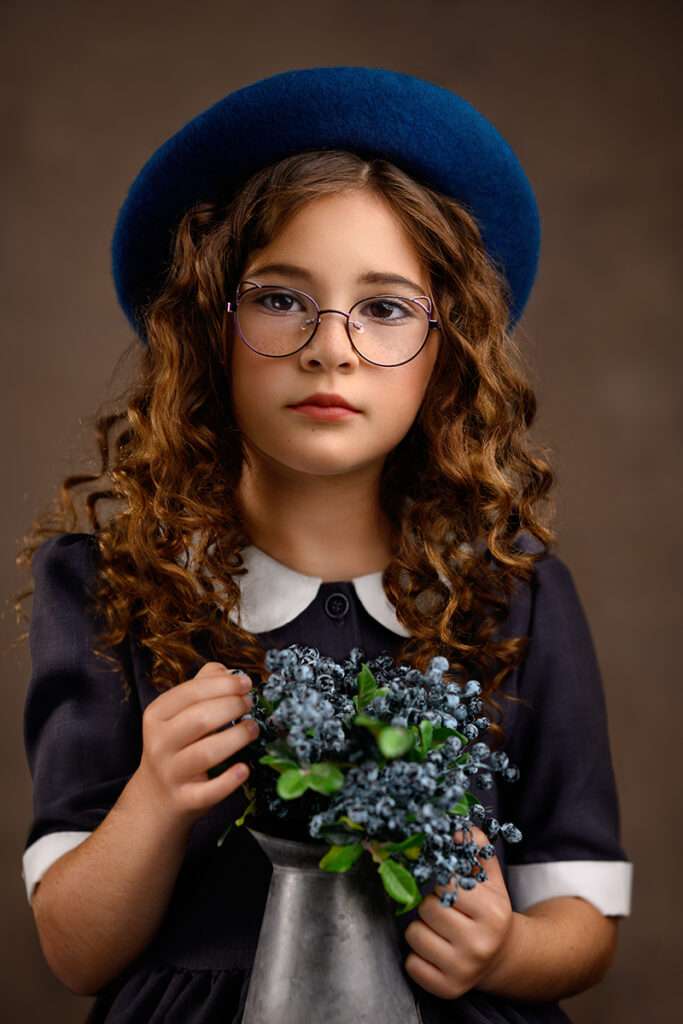 fine art portrait of a girl wearing glasses and blue beret and holding a pot with blueberries by best san diego family photographer