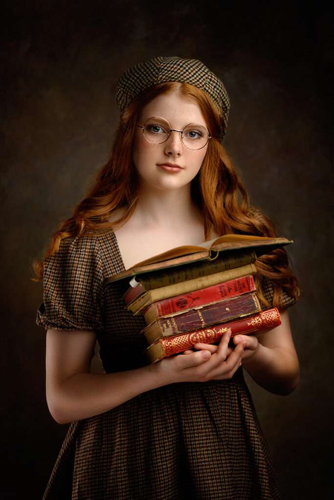 fine art studio portraits of a girl with round glasses holding books in brown vintage dress by san diego family photographer