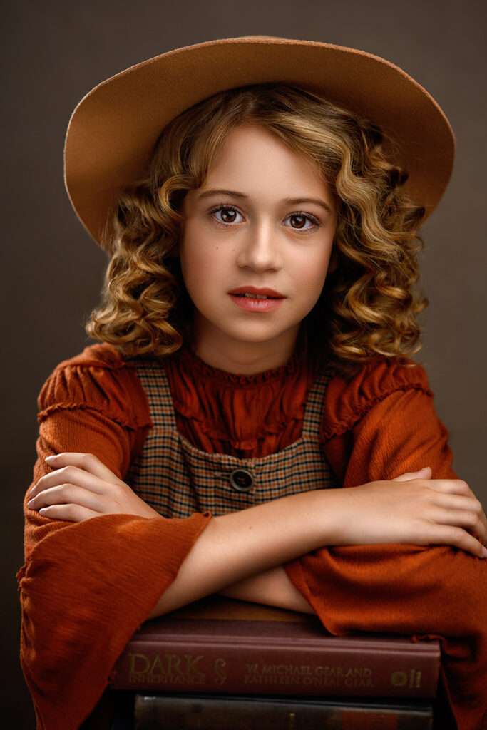 fine art portrait of a girl wearing hat and holding books photographed by best san diego family photographer