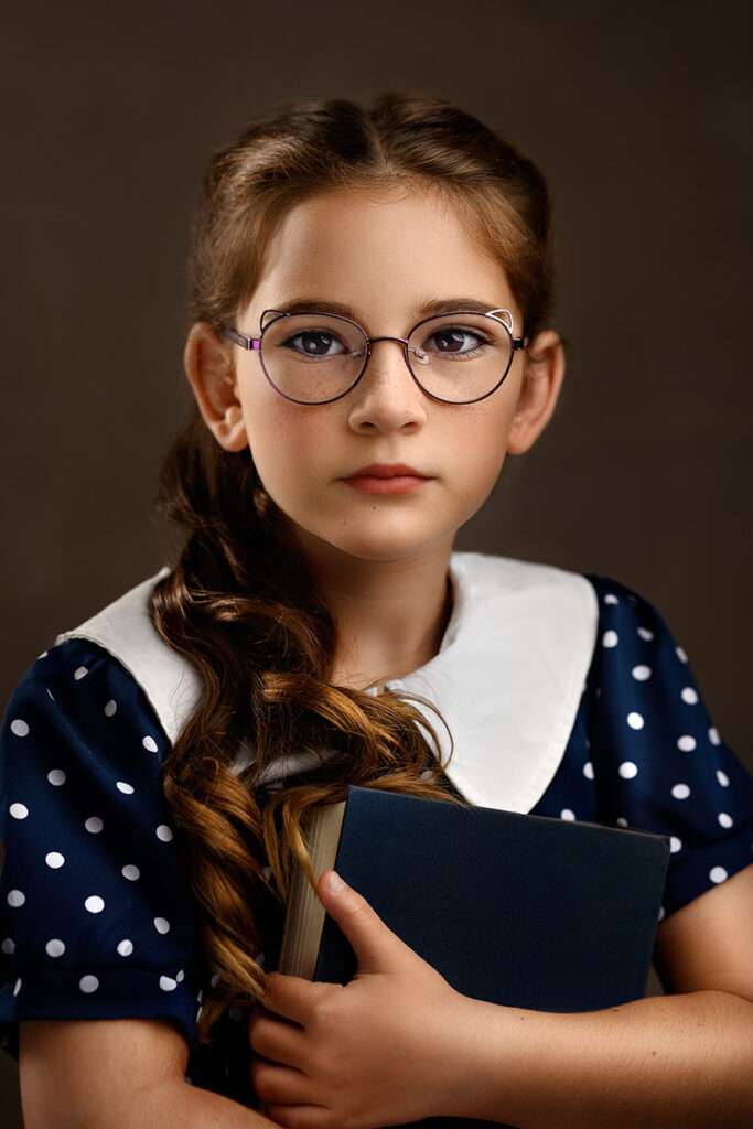 fine art portraits of a girl with glasses and blue dress holding a book by best san diego family photographer