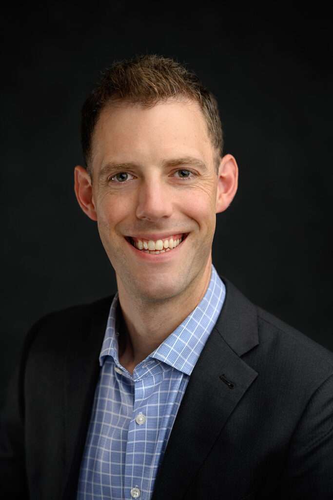 professional headshot of a men smiling with black suit and blue shirt by san diego headshot photographer